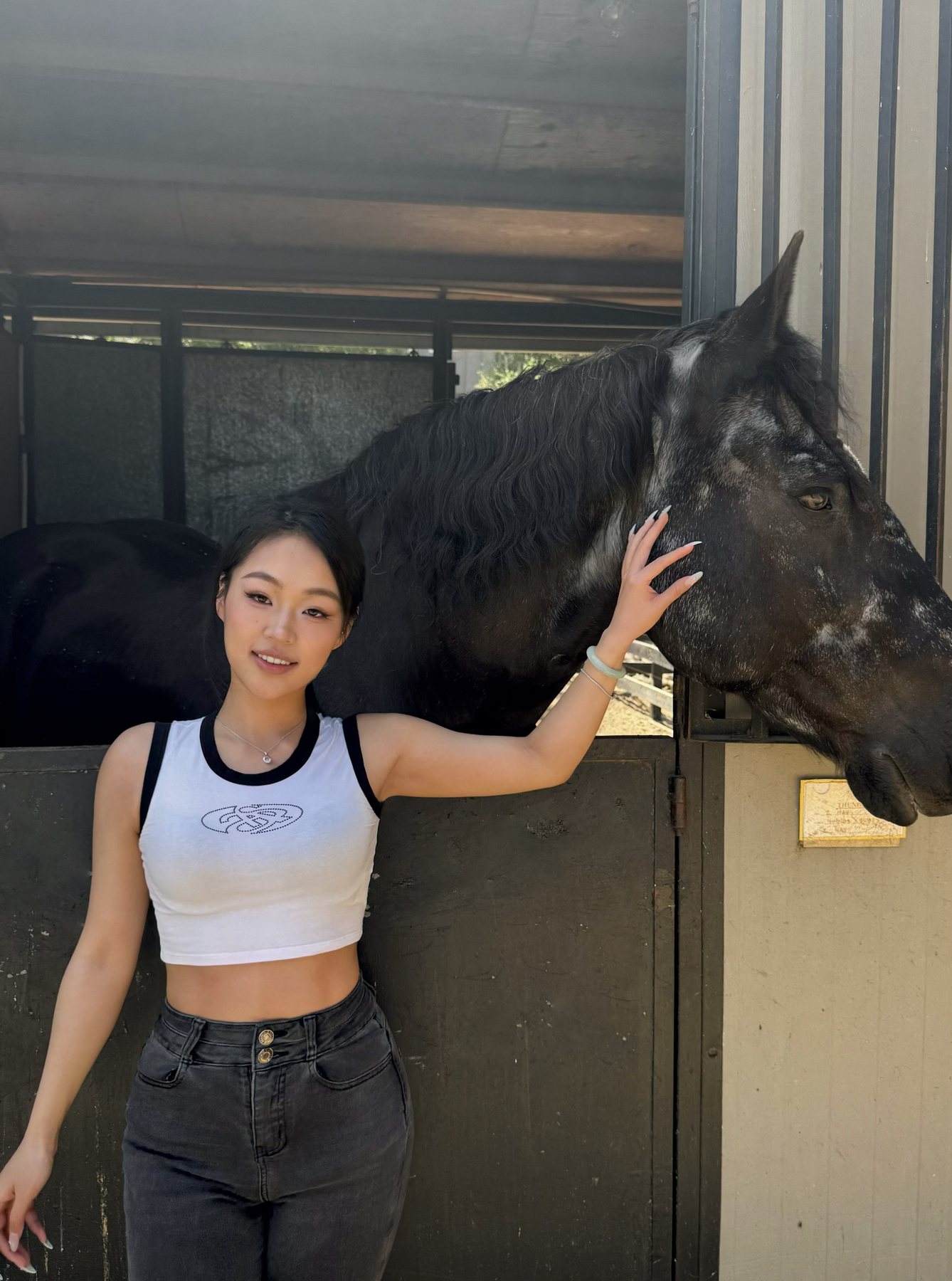 Wenyi standing beside a dark horse at a stable